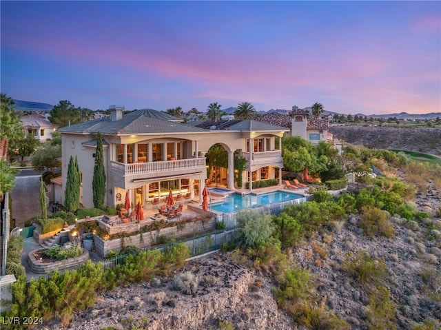 back house at dusk featuring a swimming pool with hot tub, a balcony, and a patio area