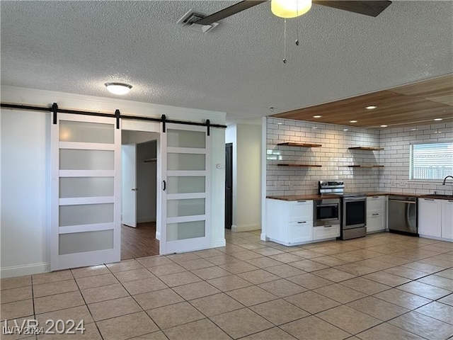 kitchen with a barn door, white cabinets, built in features, light tile patterned floors, and appliances with stainless steel finishes