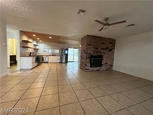 unfurnished living room with sink, a textured ceiling, a brick fireplace, ceiling fan, and light tile patterned floors