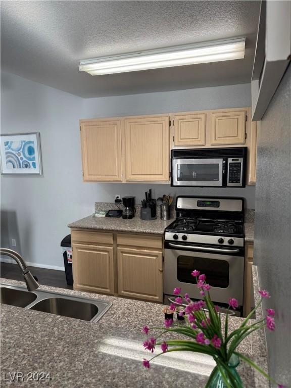 kitchen with light brown cabinets, a textured ceiling, stainless steel appliances, and sink