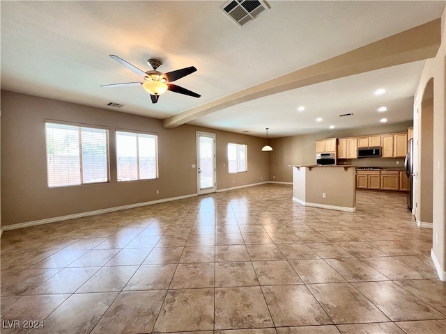 unfurnished living room featuring ceiling fan, a wealth of natural light, a textured ceiling, and beam ceiling