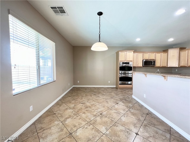 kitchen featuring light brown cabinets, stainless steel appliances, light tile patterned flooring, pendant lighting, and a kitchen bar