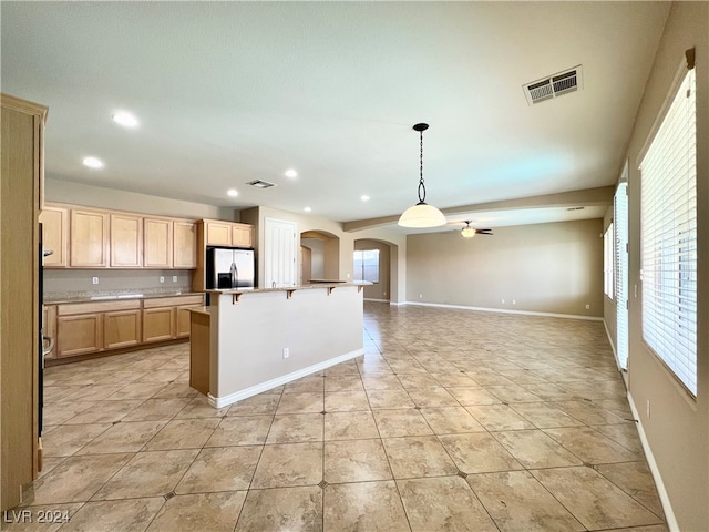 kitchen featuring hanging light fixtures, a center island with sink, stainless steel fridge with ice dispenser, a breakfast bar, and light brown cabinetry