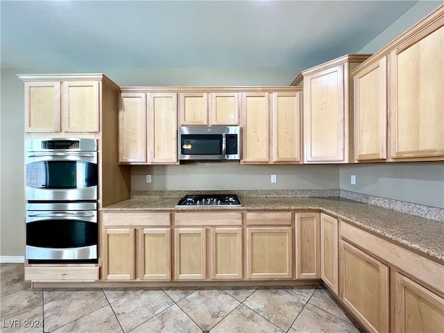 kitchen with appliances with stainless steel finishes, light tile patterned flooring, and light brown cabinets