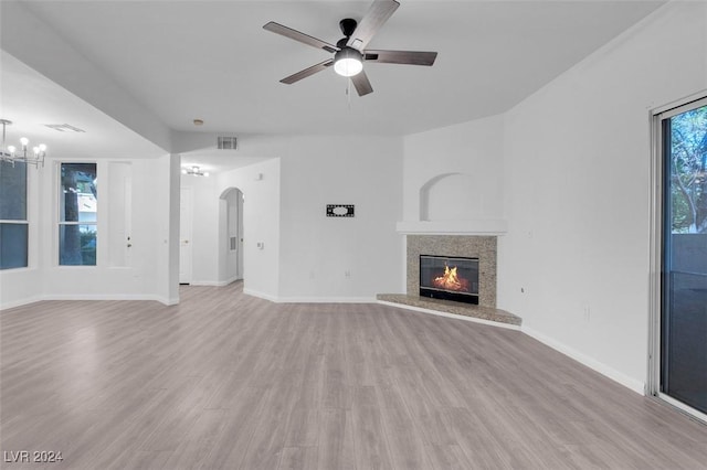 unfurnished living room featuring ceiling fan with notable chandelier, light wood-type flooring, and a fireplace