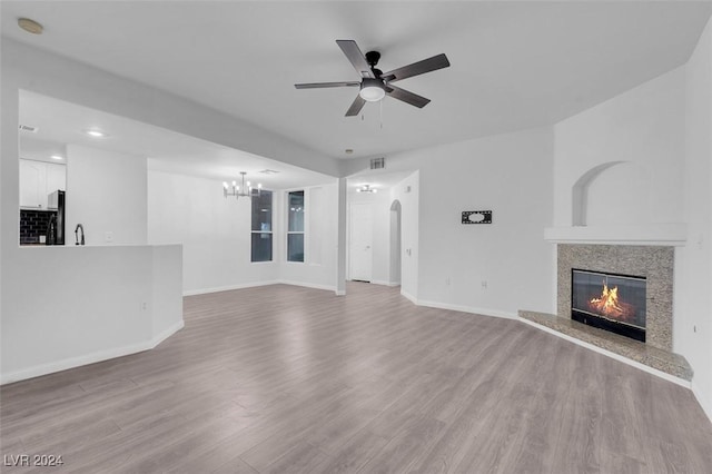 unfurnished living room featuring a fireplace, ceiling fan with notable chandelier, and light hardwood / wood-style floors