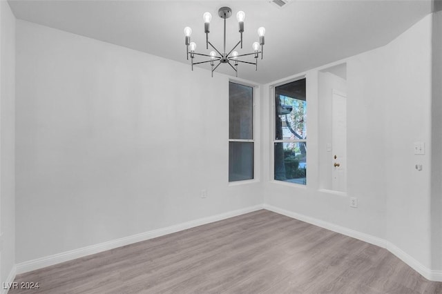 spare room with a notable chandelier and light wood-type flooring