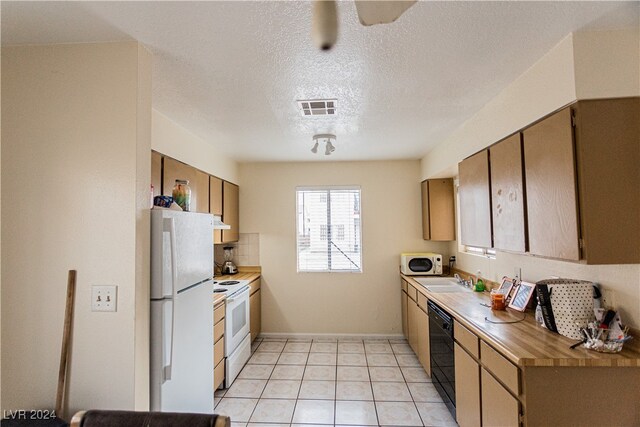 kitchen with light tile patterned flooring, white appliances, sink, exhaust hood, and a textured ceiling