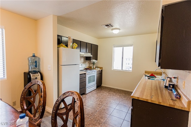 kitchen featuring backsplash, white appliances, sink, light tile patterned floors, and a textured ceiling