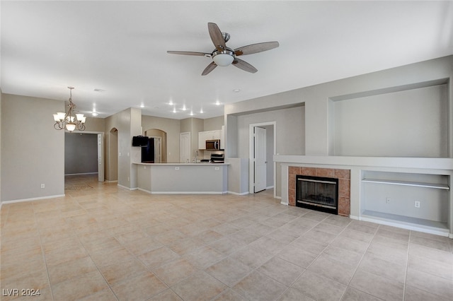 unfurnished living room with a tile fireplace, ceiling fan with notable chandelier, and light tile patterned floors