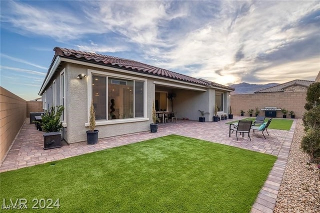 back house at dusk with a patio and a lawn