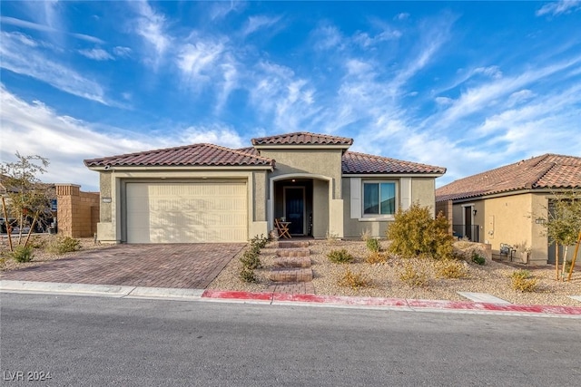 mediterranean / spanish-style house with an attached garage, decorative driveway, stucco siding, and a tile roof