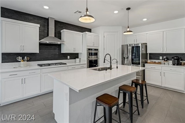 kitchen with wall chimney range hood, sink, decorative light fixtures, and appliances with stainless steel finishes