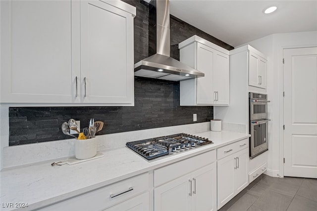 kitchen with wall chimney range hood, decorative backsplash, white cabinets, appliances with stainless steel finishes, and tile patterned floors