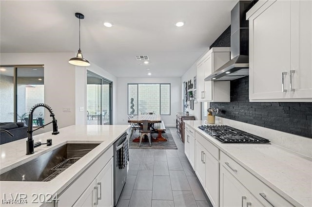 kitchen featuring wall chimney range hood, hanging light fixtures, appliances with stainless steel finishes, white cabinetry, and sink