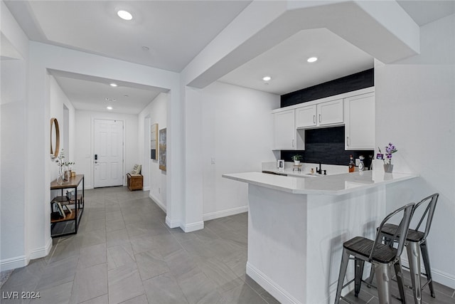 kitchen with decorative backsplash, a breakfast bar, white cabinetry, and kitchen peninsula