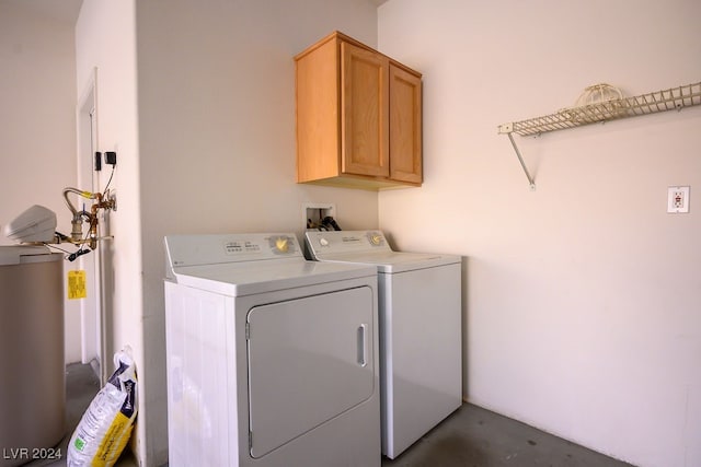 washroom featuring water heater, washer and dryer, and cabinets