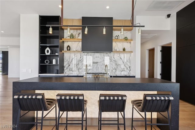 kitchen with light wood-type flooring, sink, a kitchen breakfast bar, and decorative backsplash