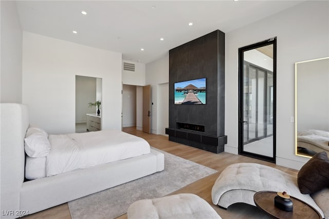 bedroom featuring a tiled fireplace, access to outside, and light hardwood / wood-style flooring