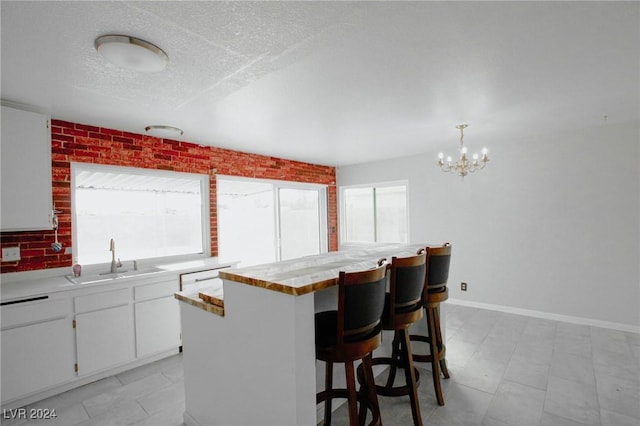 kitchen featuring sink, hanging light fixtures, a kitchen island, a kitchen breakfast bar, and white cabinets