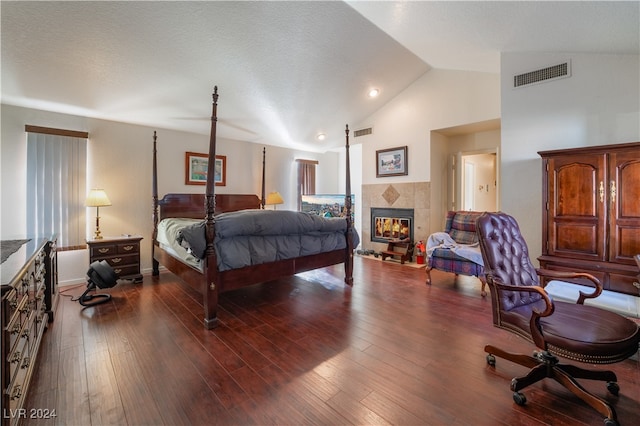 bedroom featuring dark wood-type flooring, a tiled fireplace, high vaulted ceiling, and a textured ceiling