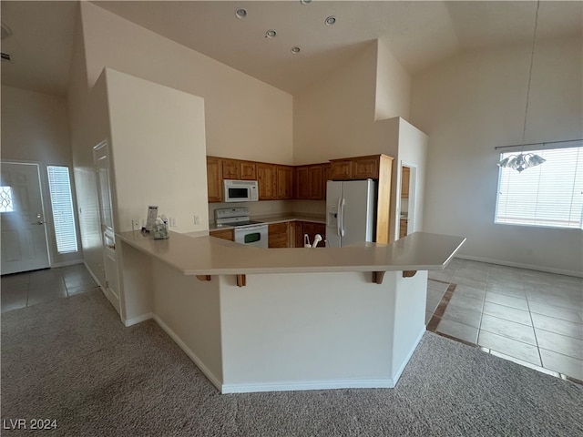 kitchen featuring kitchen peninsula, a kitchen breakfast bar, high vaulted ceiling, white appliances, and light colored carpet