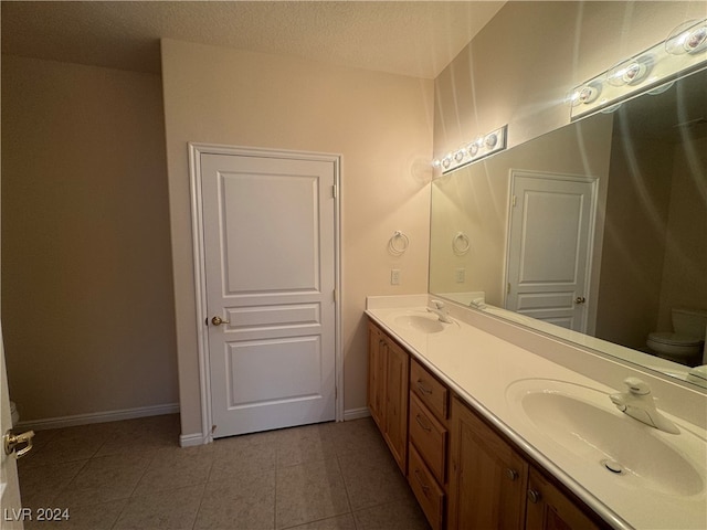 bathroom with toilet, vanity, a textured ceiling, and tile patterned floors