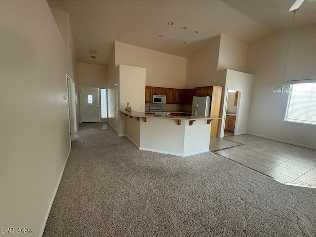 kitchen with light tile patterned flooring, a breakfast bar, kitchen peninsula, high vaulted ceiling, and white appliances