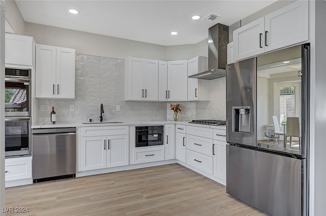 kitchen featuring a sink, white cabinetry, light countertops, wall chimney exhaust hood, and appliances with stainless steel finishes