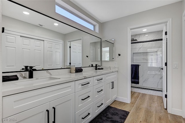 bathroom with wood finished floors, a sink, a marble finish shower, and double vanity