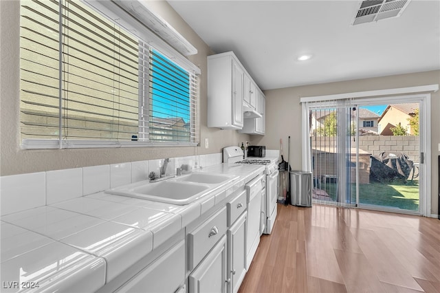 kitchen with tile countertops, white gas range oven, sink, white cabinetry, and light wood-type flooring