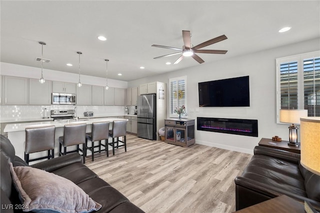 living room featuring light hardwood / wood-style flooring, ceiling fan, and sink