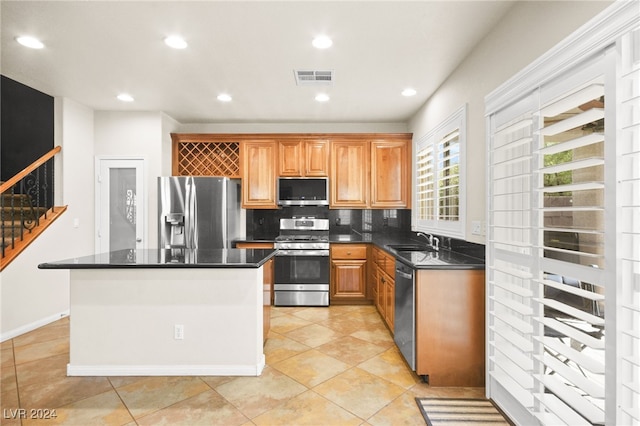 kitchen featuring tasteful backsplash, stainless steel appliances, sink, light tile patterned floors, and a kitchen island