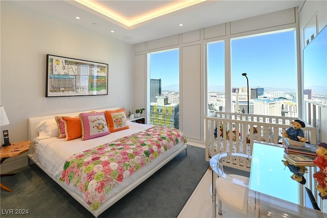 bedroom with dark colored carpet, recessed lighting, a tray ceiling, and a city view