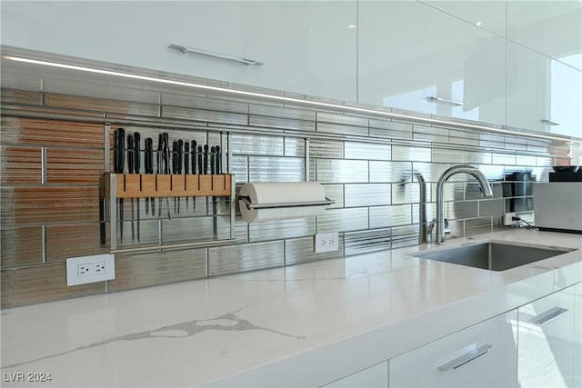 interior details with backsplash, white cabinets, light stone countertops, and a sink