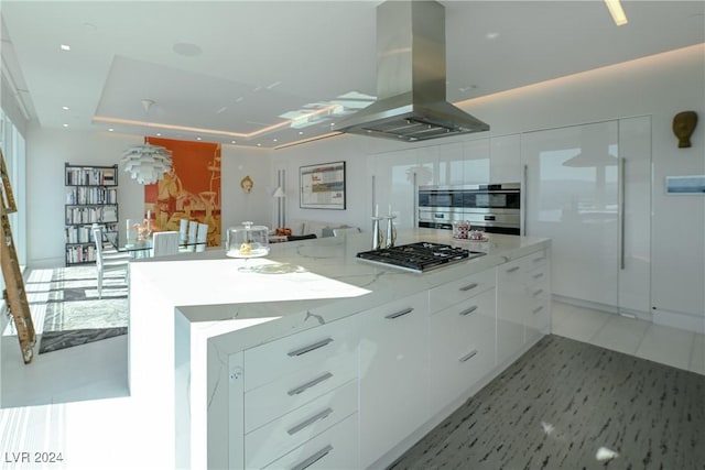 kitchen with island range hood, modern cabinets, light stone counters, stainless steel appliances, and white cabinetry
