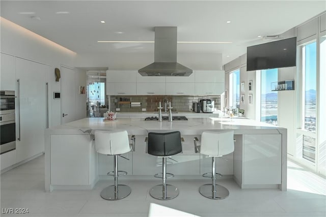 kitchen with white cabinets, decorative backsplash, island exhaust hood, a healthy amount of sunlight, and modern cabinets