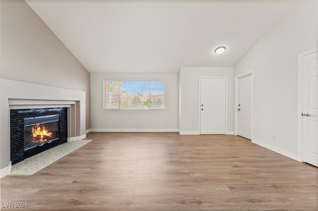 unfurnished living room featuring lofted ceiling, a tiled fireplace, and light wood-type flooring