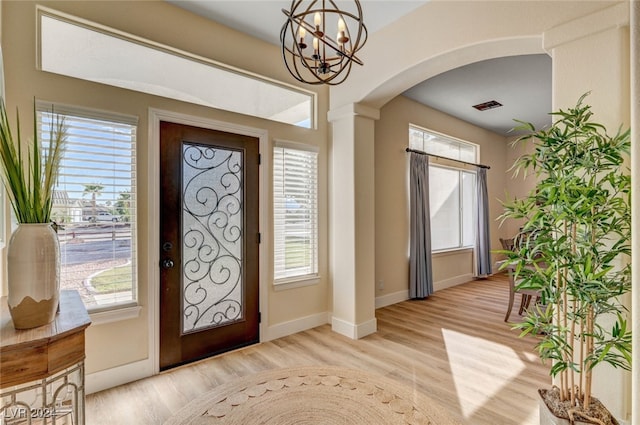 entryway featuring a wealth of natural light, a notable chandelier, ornate columns, and light wood-type flooring