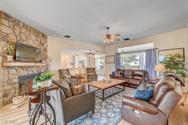 living room with a stone fireplace, light hardwood / wood-style flooring, and ceiling fan