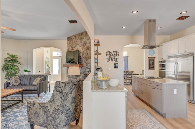 kitchen with light stone counters, white cabinetry, island range hood, light hardwood / wood-style floors, and stainless steel appliances