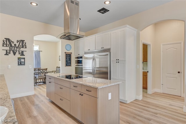 kitchen with island exhaust hood, light stone counters, appliances with stainless steel finishes, light hardwood / wood-style floors, and a center island