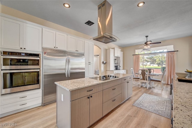 kitchen with island range hood, light hardwood / wood-style flooring, white cabinets, appliances with stainless steel finishes, and light stone counters