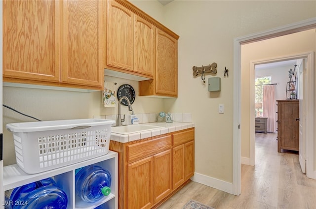 laundry room featuring sink, light wood-type flooring, and cabinets