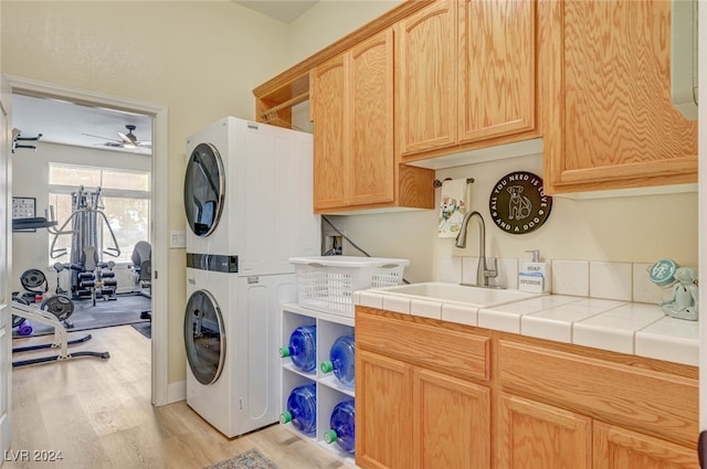 washroom featuring cabinets, ceiling fan, stacked washing maching and dryer, light hardwood / wood-style flooring, and sink