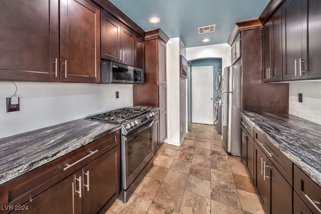 kitchen with dark brown cabinetry, stainless steel appliances, and dark stone countertops