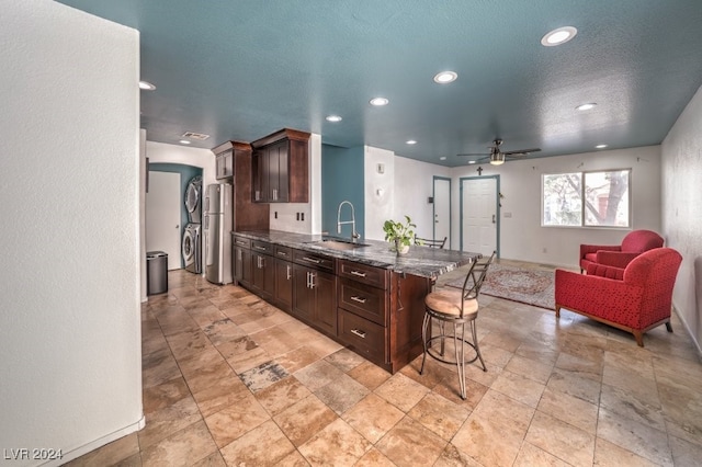 kitchen featuring stainless steel fridge, a breakfast bar, stacked washer / drying machine, dark brown cabinetry, and sink