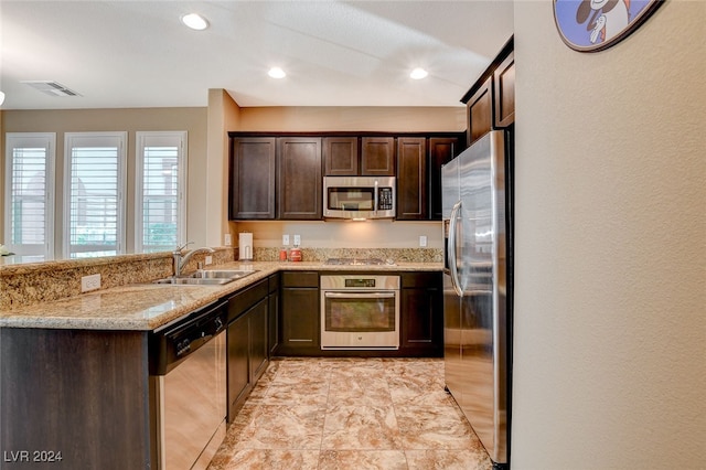 kitchen with light stone countertops, sink, appliances with stainless steel finishes, and dark brown cabinetry