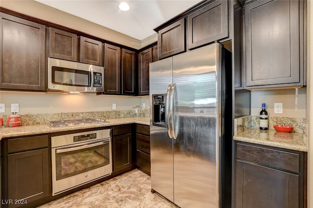 kitchen with dark brown cabinetry, stainless steel appliances, and light stone countertops