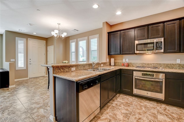 kitchen with appliances with stainless steel finishes, sink, dark brown cabinets, kitchen peninsula, and pendant lighting